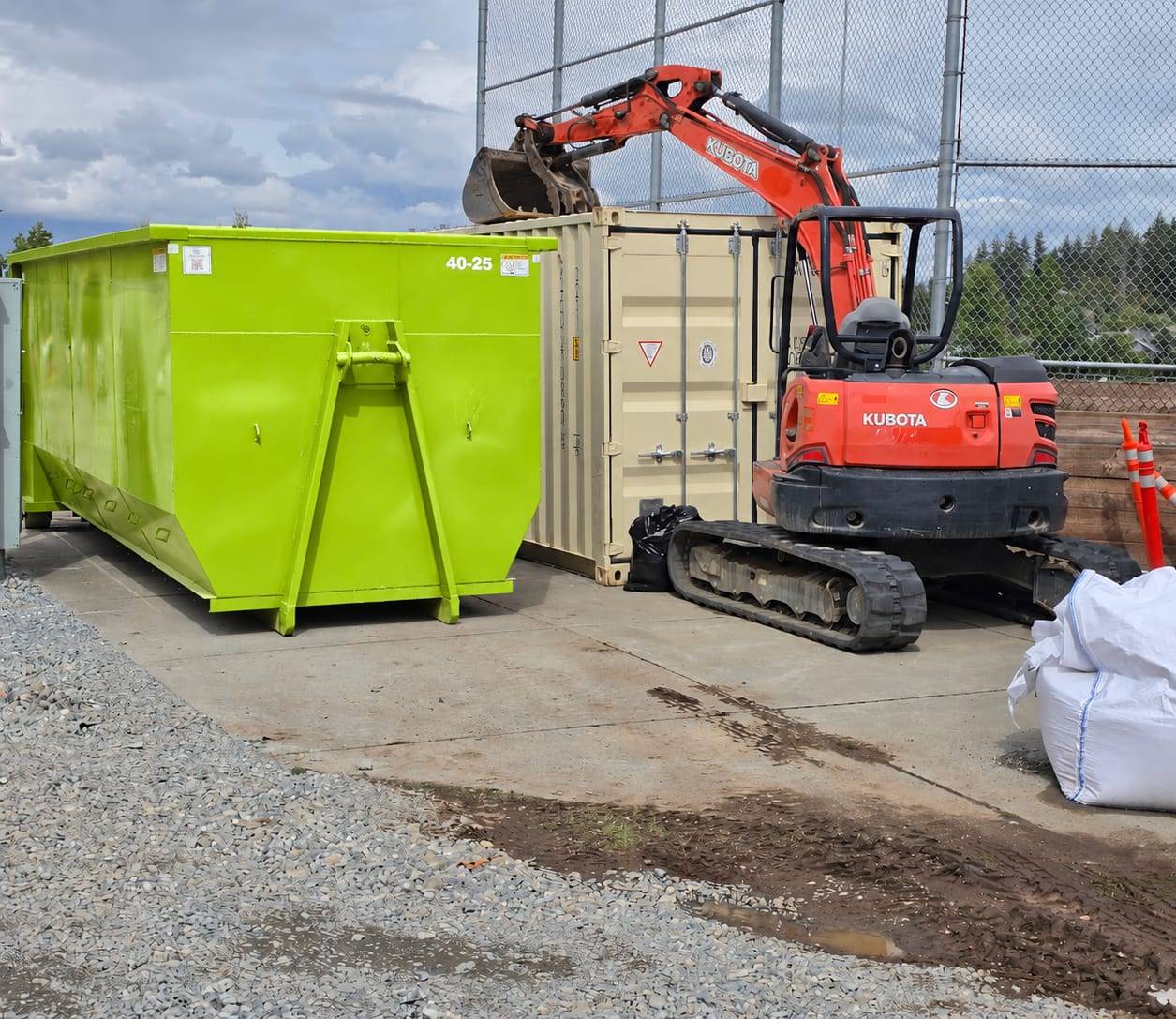 Lime green roll-off container beside a mini excavator at a commercial construction site