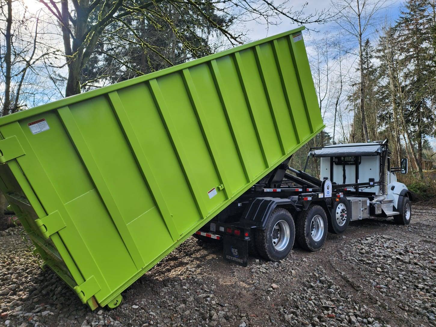 Rainier Dumpster Rental roll-off truck setting a lime green dumpster on a gravel pad in Seattle