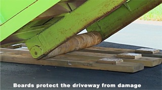 A close-up of a roll-off dumpster's steel wheel resting on protective wood dunnage on a residential driveway.